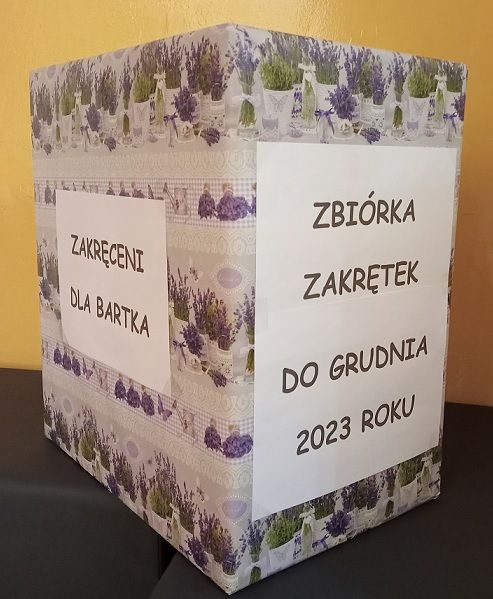 Karton do którego zbierane są nakrętki w akacji " Zakręceni dla Bartka". Na kartonie znajduje się kartka z napisem " Zbiórka zakrętek do grudnia 2023".