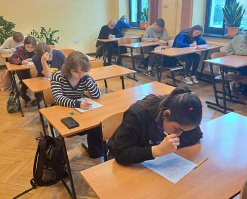 Uczniowie siedzą w klasie w ławkach podczas rozwiązywania zadań konkursowych.