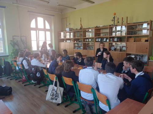Uczniowie klasy 1 w klasie. Siedzą przy połaczonych stolikach na których znajdują się ciasta i napoje. Zdjęcie 1.